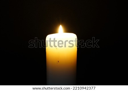 A white candle light burning in the dark