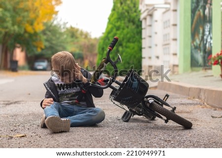 Preschool boy hurts his forehead after falling off his bicycle. Child is learning to ride a bike. the boy hit his head on the asphalt Royalty-Free Stock Photo #2210949971