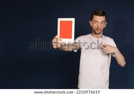 A man in a white T-shirt standing on a blue background holding a tablet, advertising shot