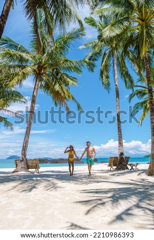 Men and women in swim shorts walking on a white tropical beach in Thailand, Koh Kham Trat. men in swim short and Asian women on the beach with palm trees and white sand