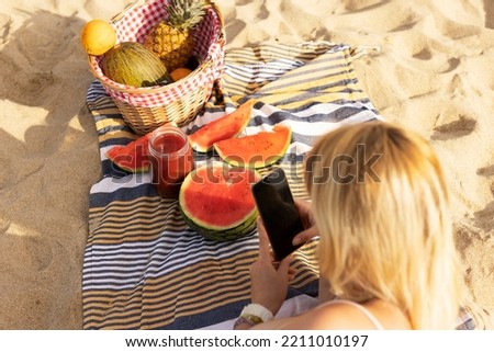 Cheerful young woman enjoy at tropical sand beach. Young woman taking a picture of fruit on the beach.