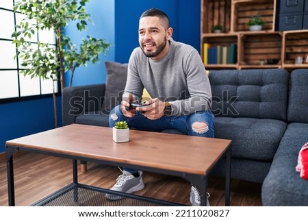 Young latin man playing video game sitting on sofa at home