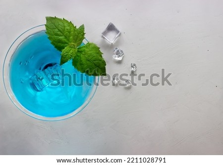 Top view of blue cocktail in martini glass with ice cubes and mint