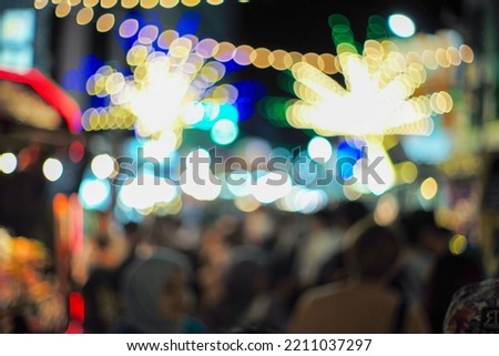 Blurred ground of bokeh lights decorated in the night flea market with shadow of crowded people in foreground. Picture was defocused in purpose.