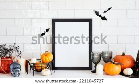 Halloween holiday concept. Scandinavian living room interior with picture frame mockup, Halloween home decor, pumpkins on white desk table. Halloween poster template.