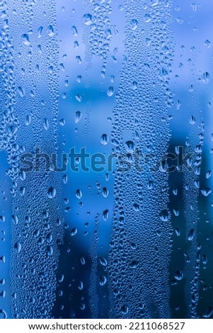 Close-up of raindrops on a window pane. Gloomy wet weather. Drops of water on glass in front of dark blue rain clouds. Rain. Abstract background texture