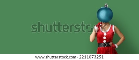 Young woman in Santa Claus costume and with Christmas ball instead of her head on green background with space for text