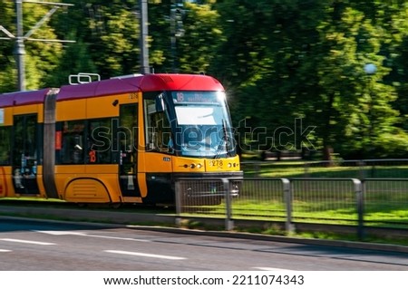 A yellow Warsaw tram driving by with natural motion blur seen from the front with green trees in the background Royalty-Free Stock Photo #2211074343