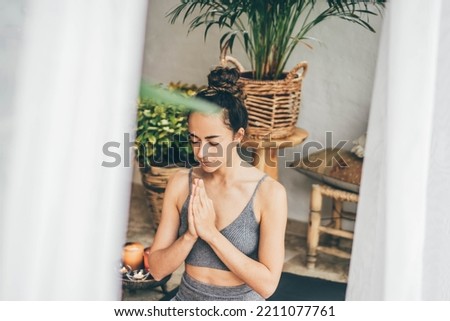 Young woman sitting in the lotus position on floor in a cozy boho room.