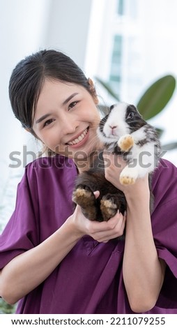 Smiling asian veterinary holding easter rabbit in her arm in modern clinic or animal hospital
 Happy asian woman and healthy rabbit.
