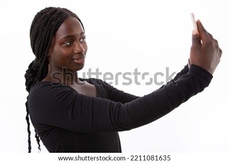 Portrait of happy young woman taking selfie with smartphone against white background. Braided African American lady wearing longsleeve posing at mobile camera. Social networking concept