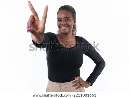 Portrait of cheerful young woman making rock gesture against white background. Successful African American lady wearing black longsleeve looking at camera and smiling. Success and happiness concept