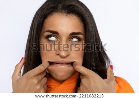 Young Hispanic woman stretching mouth with fingers. Female model in orange hoodie grimacing, making funny faces, rolling up eyes. Portrait, studio shot, grimacing concept