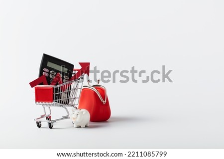 Miniature Shopping cart trolley, piggy bank, calculator, coin purse and red arrow up on white background with copy space. Concept for grocery expenses and consumerism