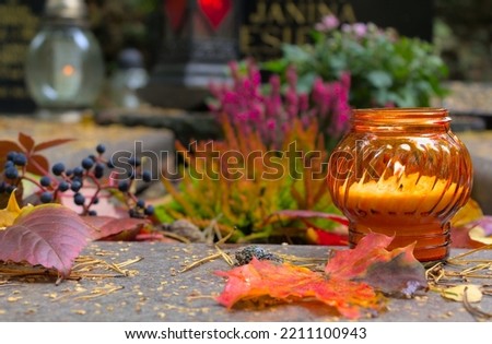An orange candle on a grave in a cemetery on an autumn day. All Saints Day. Copy space, shallow depth of field. Royalty-Free Stock Photo #2211100943