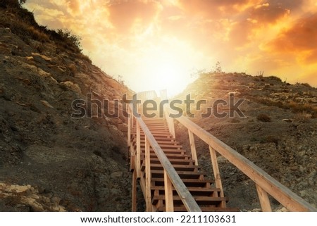 Religion and motivation. A wooden steep staircase in the mountain leading to the sky, with bright sunlight and sunset. Bottom view. The concept of paradise, victory and hope for a bright future. Royalty-Free Stock Photo #2211103631