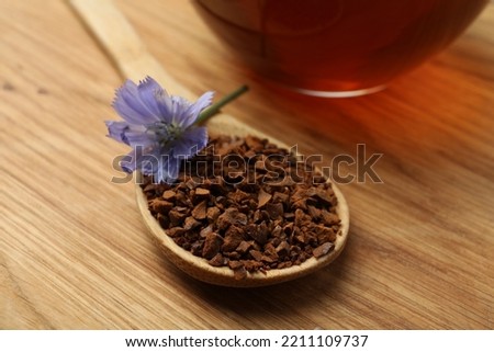 Spoon of chicory granules with flower on wooden table, closeup