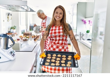 Middle age hispanic couple smiling happy baking cookies at the kitchen.