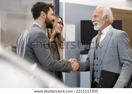 Young couple looking to buy a new car. Car salesman making a sale. Signing a papers for purchase a new car
