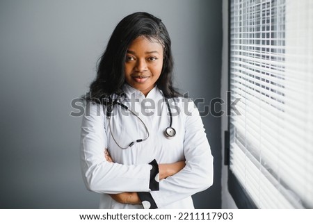 Portrait confident African female doctor medical professional writing patient notes isolated on hospital clinic hallway windows background. Positive face expression