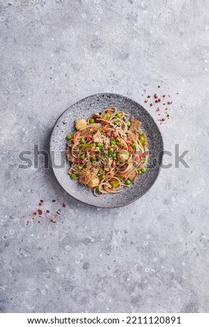 Wok with turkey meat, soba noodles, corn, green peas, green beans and carrots served on gray background with chopsticks. Asian food, concept of street food. Top view with copy space Royalty-Free Stock Photo #2211120891