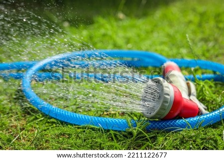 Water spraying from hose on green grass outdoors, closeup Royalty-Free Stock Photo #2211122677