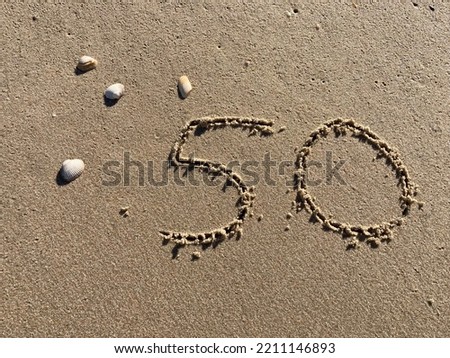 On the beach in the sand is carved the number 50