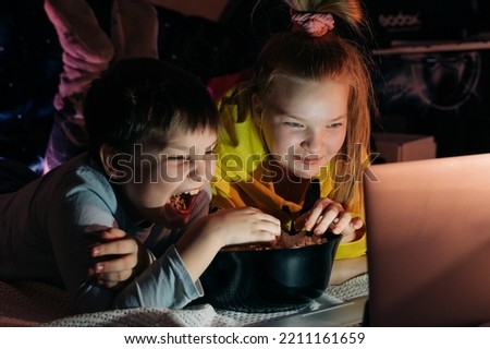 Overjoyed Kids sister brother laughing spend weekend free time together at home on couch bed eating popcorn. teen children watching video cartoon use remote control on laptop have fun. Movie night