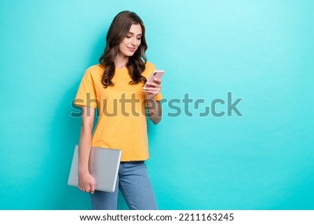 Photo of young successful pretty nice girl hold computer typing new smartphone text empty space ad youtube blogger isolated on aquamarine color background