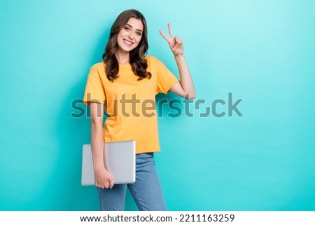 Photo of young attractive cute nice pretty woman wear orange t-shirt hold laptop showing v-sign empty space ad app for dating isolated on cyan color background