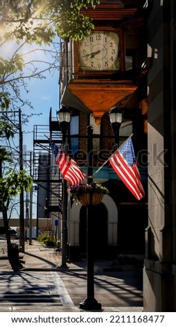The morning sun shines on flags below a large clock in the downtown district of Manitowoc, Wisconsin.