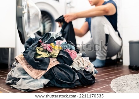 Laundry, washing clothes. Man loading washer machine and sorting by color and fabric.  Male homemaker doing house chores. Domestic work in family. Young dad and parent putting clothing in dryer. Royalty-Free Stock Photo #2211170535