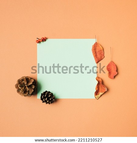 Pine cone, orange natural leaf, red decoration on orange background with green card for greetings. Minimal autumn concept with copy space. Creative flat lay idea. Season of colorful fall vibe.