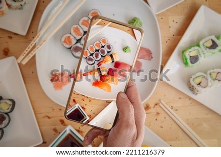 Man with mobile phone taking photo of delicious sushi on table, top view