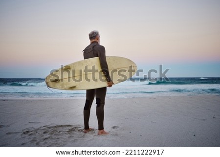 Surfer, surfboard and senior man on beach at sea waves in during sunset during summer vacation in Hawaii. Professional male athlete rest after training or practice surfing sport outdoor at the ocean