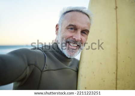 Beach, selfie and happy senior surfer in retirement with surfboard training by the ocean. Happiness, freedom and portrait of an elderly man with smile taking picture while surfing on tropical holiday