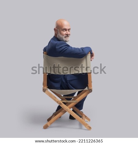 Confident film director sitting on the director's chair and looking at camera: video production, filmmaking and film industry concept Royalty-Free Stock Photo #2211226365