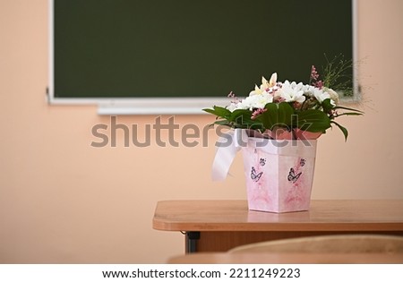 a bouquet of flowers with a white gift bow on the background of a school board in an empty classroom. teacher gift concept.