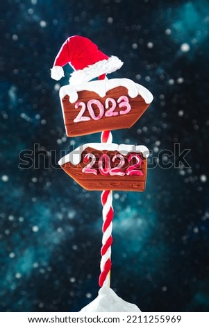 Wooden 2023 and 2022 direction signs and Santa's hat against the night starry sky. In anticipation of the New Year 2023.