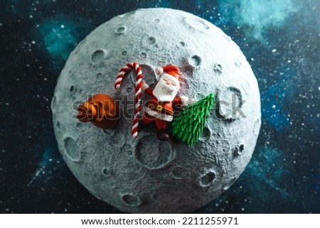 Plasticine Santa Claus lies on the moon with a bag of gifts and a Christmas tree. Christmas card.