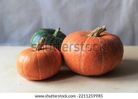 Three fresh small ripe pumpkins of different varieties and sizes, two orange and one green, lie as a group on a light wood table. Autumn harvest. Preparation for Halloween. Image with selective focus
