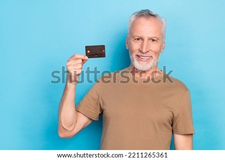 Photo of optimistic satisfied pensioner gray hairstyle stubble wear beige t-shirt hold debit card isolated on blue color background
