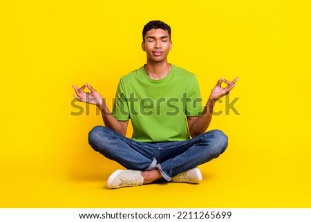 Full length photo of cute dreamy guy wear green t-shirt sitting floor practicing yoga isolated yellow color background