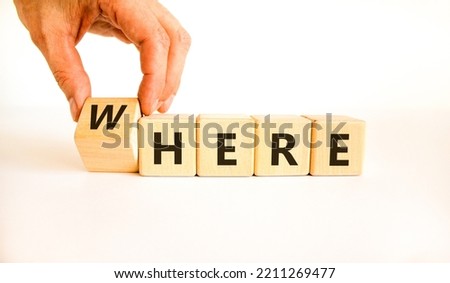 Where or here symbol. Businessman turns a wooden cube, changes the word 'where' to 'here'. Beautiful white table, white background, copy space. Business, where or here concept.