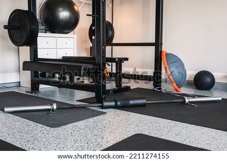 Indoor garage gym setup with home exercise and fitness equipment. Lifting rack, bench and bar ready for use. Home gym with natural light.  Royalty-Free Stock Photo #2211274155