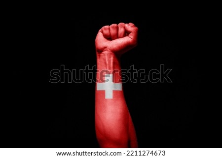 Strong man's hand in battle signal with Swiss flag on black background.