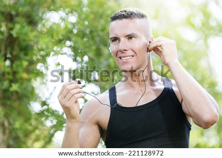 Young man wears headphones to listen music before starting fitness training in the park.