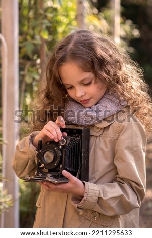 Portrait of young beautiful child with retro camera. Little girl with old photography camera in hands outdoors. Child hobby and  education. Kid and photography. Selective focus, close up.
