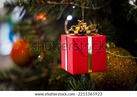 Large red color box surprise Yellow ribbon bow bokeh background. Gift for holiday in winter December. Green branch tree with ball decoration. Happy New Year. Merry Christmas