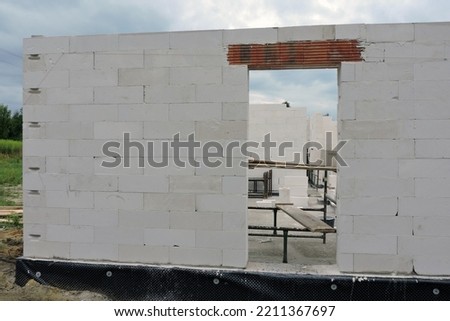 A house under construction, walls made of acc blocks, a rough door opening, reinforced brick lintels, a scaffolding, insulated foundation walls, solid concrete blocks and acc blocks Royalty-Free Stock Photo #2211367697